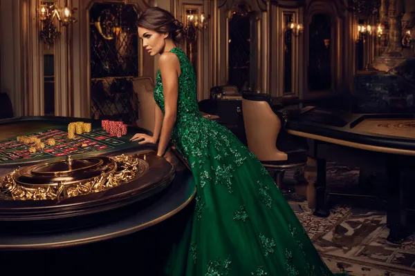 GOOD111 — A high-class gaming experience without limits A woman in a luxurious green gown next to an ornate roulette wheel, capturing the upscale casino mood of GOOD111.